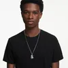 A young man wearing a black t-shirt and a silver necklace with a rectangular blue pendant. Produktbild-Vorschau