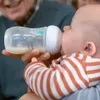 A person is feeding a baby with a bottle. Produktbild-Vorschau