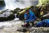 A man is filtering water from a stream near a waterfall. Produktbild-Vorschau