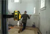 A man is kneeling on a wooden floor, using a laser level to mark a wall in a room under renovation. Produktbild-Vorschau