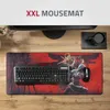 A desk setup with a large mousepad, keyboard, and mouse, with a monitor in the background. Produktbild-Vorschau