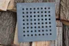 A square cast iron grate with many circular holes sits on a pile of chopped wood. Voir les images du produit
