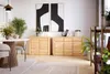 A modern living room scene featuring two wooden sideboards, a dining table, chairs, plants, and artwork. Produktbild-Vorschau