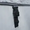 A close-up of a black plastic buckle and black nylon strap attached to a gray fabric edge of a white product. Podgląd zdjęcia produktu