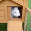 A white rabbit peeking out of a wooden hutch with a wire mesh enclosure. Produktbild-Vorschau