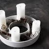 A concrete candle holder with four white candles, pine cones, and dark spheres on a dark wooden floor. Voir les images du produit