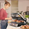 A woman is preparing food on a panini press in a kitchen. Podgląd zdjęcia produktu