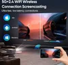 A projector is shown in a living room setting, casting an image onto a wall. A smartphone is also shown displaying the same image, indicating screencasting capabilities. Produktbild-Vorschau