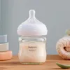 A baby bottle filled with milk sits on a wooden surface, with soft blankets and blocks in the background. Náhľad obrázku produktu