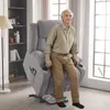 An elderly man is sitting in a gray lift recliner chair next to a bookshelf. The chair has cup holders and a side pocket with a remote control. Podgląd zdjęcia produktu