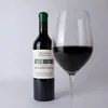 A bottle of red wine and a glass of red wine are placed on a light gray background. Produktbild-Vorschau