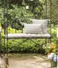 A garden bench with cushions and pillows, surrounded by greenery and flowers. Produktbild-Vorschau