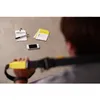 A person is holding a TRX suspension trainer, with a smartphone and some cards on the floor nearby. Produktbild-Vorschau