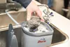 A hand is shown placing a glass into a washing device in a sink. Podgląd zdjęcia produktu