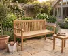 Massive Teakholzbank Picadelly 150 cm in Natur mit vertikalen Lamellen und Armlehnen, Gesamtansicht im Garten. Produktbild-Vorschau