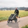 A man is jogging with a child in a stroller on a path in a park. Produktbild-Vorschau