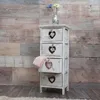 A vintage-style white chest of drawers with heart cutouts, set against a distressed wooden plank wall. Anteprima dell’immagine prodotto