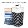 A folded laundry basket with a black and white pattern stands next to a stack of folded clothes. Produktbild-Vorschau