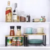 A two-tiered kitchen shelf organizer holding various items like spice grinders, cans, cups, and plates, arranged on two shelves within a cabinet. Produktbild-Vorschau