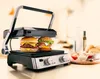 A grill with two burgers on it, set on a kitchen counter with some condiments and bread rolls. Podgląd zdjęcia produktu