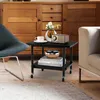 A modern side table with decorative items on top and books on the shelf, placed next to a chair and in front of a wooden cabinet. Produktbild-Vorschau