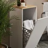 A bathroom cabinet with a laundry basket inside, next to a potted plant. Voir les images du produit