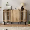 A wooden sideboard with slatted doors and black legs, decorated with a lamp, a framed picture, and a vase with a plant. Anteprima dell’immagine prodotto