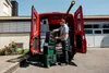 A man is loading toolboxes from the back of a red van. Produktbild-Vorschau