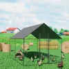 A chicken coop with chickens and hay bales in a grassy field with houses and trees in the background. Anteprima dell’immagine prodotto