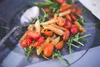 A close-up of penne pasta with cherry tomatoes and arugula on a dark plate, with a spoon. Produktbild-Vorschau
