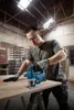 A man is using a jigsaw to cut a piece of wood in a workshop. Anteprima dell’immagine prodotto