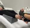 A person's feet are being treated with a pedicure device. The foot is resting on a gray footrest. There are bottles of products in the background. Náhled obrázku produktu
