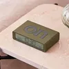 A khaki-colored digital alarm clock with the word "on" embossed on its top surface, placed on a marble-patterned surface. Náhľad obrázku produktu