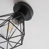 A close-up view of a black, geometric cage-style ceiling light fixture with a clear Edison-style bulb inside. Produktbild-Vorschau