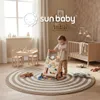 A baby is playing with a wooden walker in a nursery room with a crib and a small table and chairs. Produktbild-Vorschau