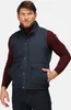 A man wearing a navy blue quilted vest over a burgundy turtleneck and dark wash jeans. Voir les images du produit