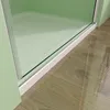 A close-up view of the bottom edge of a shower enclosure, showing the glass door, white frame, and the wooden floor outside. Produktbild-Vorschau