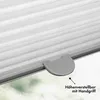 Close-up of a gray pleated blind with a handle, showing a detail of its height adjustment mechanism against a blurred green and white background. Produktbild-Vorschau