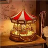 A detailed shot of a wooden carousel model with LED lights, set on a wooden table with a floral wallpaper background. Produktbild-Vorschau
