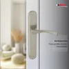 A close-up of a nickel-colored door handle on a white door, with a blurred interior scene in the background. Produktbild-Vorschau