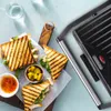 A close-up shot of a grill with sandwiches and condiments. Produktbild-Vorschau