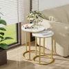 Two nesting round side tables with marble-look tops and gold metal frames are placed next to a sofa, with a bouquet of flowers on the larger table. Náhled obrázku produktu