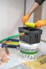 A person is cleaning a paint roller with a hose connected to a washing device that sits on top of a bucket. Náhled obrázku produktu