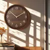 A wooden wall clock with golden numbers is hanging on a wall, with sunlight casting shadows. Voir les images du produit