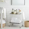 A white rolling cart with two shelves filled with folded white towels and bathroom products is shown in a bathroom setting. Voir les images du produit