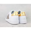 A rear view of a pair of white Adidas sneakers with gold accents. Produktbild-Vorschau