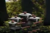 A collection of cookware set arranged on a mossy forest floor with trees in the background. Produktbild-Vorschau