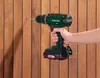 A hand holding a cordless drill and drilling into a wooden wall. Produktbild-Vorschau