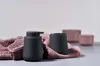 A black ceramic soap dispenser and toothbrush holder sit on a pink textured towel, with two pink ceramic containers in the background. Produktbild-Vorschau