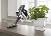 A cordless vacuum cleaner is displayed on a wooden countertop next to a potted plant. Produktbild-Vorschau